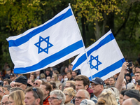 Teilnehmer der Kundgebung „Aufstehen gegen Terror, Hass und Antisemitismus – in Solidarität und Mitgefühl mit Israel“ stehen umhüllt in eine israelische Flagge vor dem Brandenburger Tor in Berlin. - Foto: Monika Skolimowska/dpa