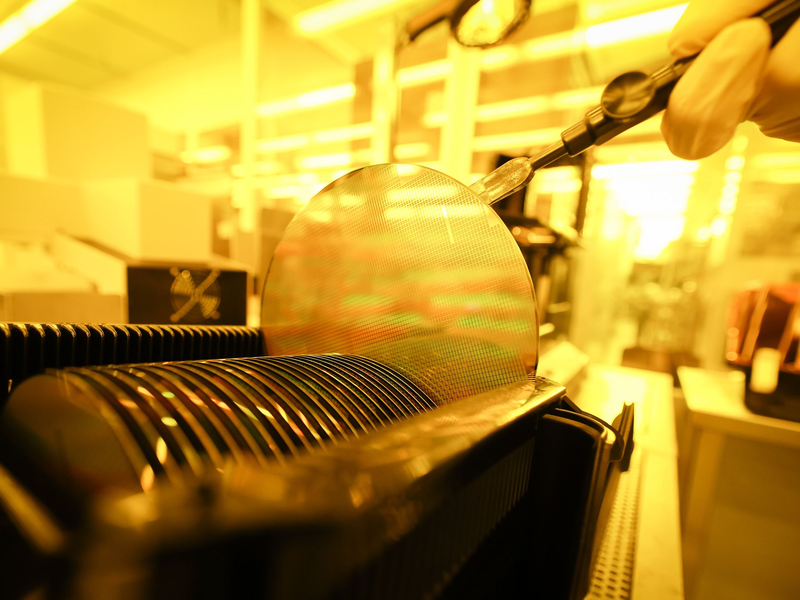 Ein Mitarbeiter in der Produktion von Wafern arbeitet unter Gelblicht im Reinraum. Die deutsche Wirtschaft leidet noch immer unter gravierenden Lieferengpässen der weltweiten Chipindustrie. - Foto: Christian Charisius/dpa