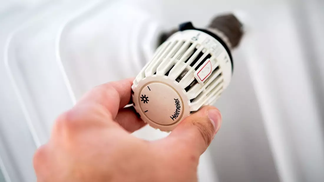 Ein Mann dreht in einer Wohnung am Thermostat einer Heizung. - Bild: Hauke-Christian Dittrich/dpa