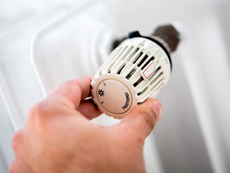 Ein Mann dreht in einer Wohnung am Thermostat einer Heizung. - Foto: Hauke-Christian Dittrich/dpa