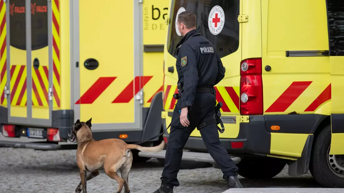Ein Polizist läuft nach einer eingegangen Drohung mit einem Hund vor einer Grund- und Oberschule im ostsächsischen Pulsnitz: Ähnliche Einsätze gibt es heute in Thüringen und Baden-Württemberg. - Bild: Rocci Klein