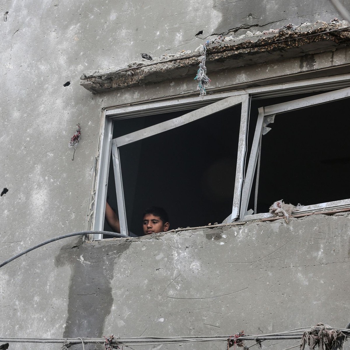 Ein kleiner palästinensischer Junge blickt aus dem Fenster eines zerstörten Gebäudes. - Foto: Mohammed Talatene/dpa