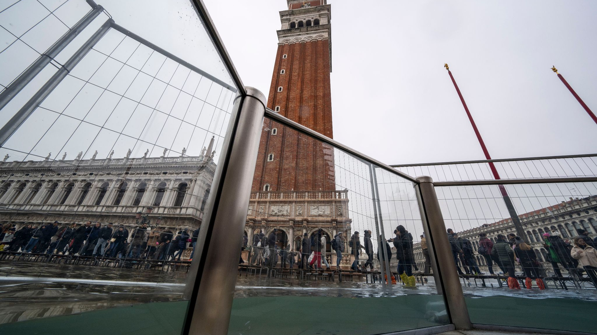 Touristen gehen auf Laufstegen über den überschwemmten Markusplatz. - Foto: Domenico Stinellis/AP/dpa