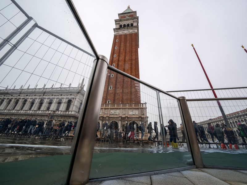 Touristen gehen auf Laufstegen über den überschwemmten Markusplatz. - Foto: Domenico Stinellis/AP/dpa
