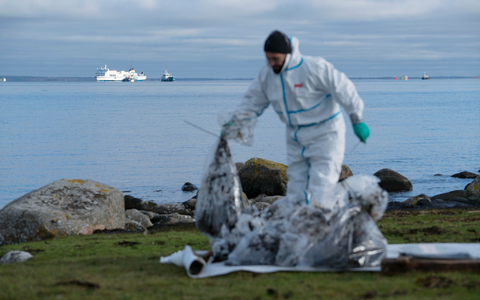 Ein Mann in Schutzkleidung arbeitet am Strand. Bei der vor der südschwedischen Küste feststeckenden Ostseefähre «Marco Polo» (hinten, l) ist erneut Öl ausgetreten. - Foto: Ola Torkelsson/TT News Agency/AP/dpa