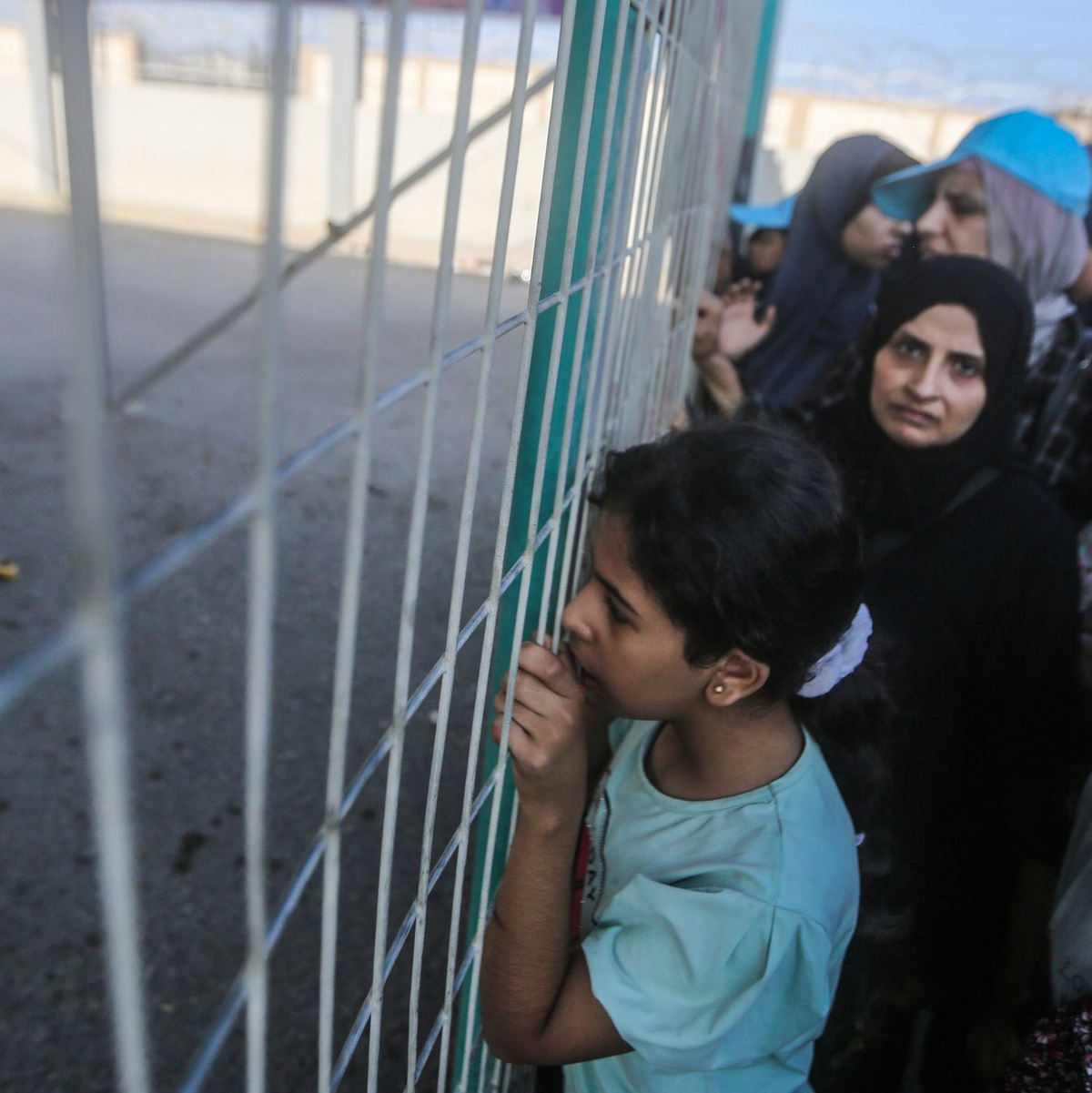 Menschen warten vor einem Zaun am Grenzübergang zwischen dem Gazastreifen und Ägypten. - Foto: Mohammed Talatene/dpa