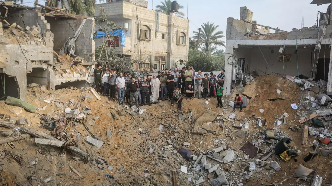 Palästinenser stehen in Chan Junis im Gazastreifen um einen Krater herum, der durch einen israelischen Angriff verursacht wurde. - Bild: Mohammed Talatene/dpa