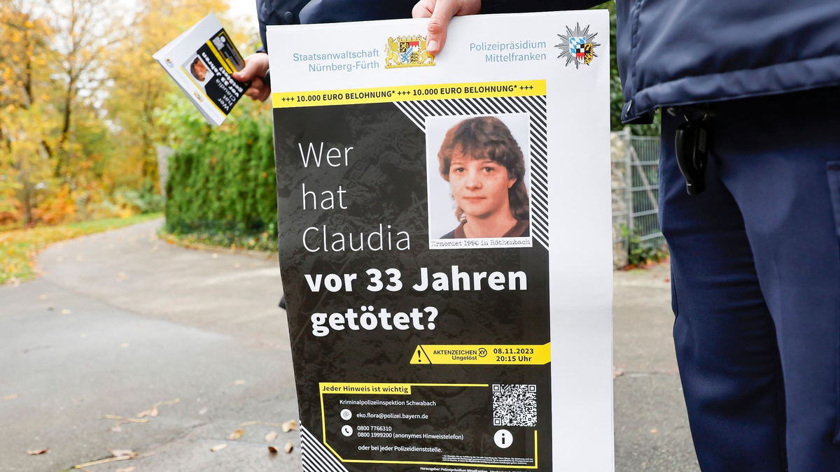 Ein Polizist mit einem Plakat zum Mordfall von 1990 in Röthenbach an der Pegnitz. - Foto: Daniel Löb/dpa
