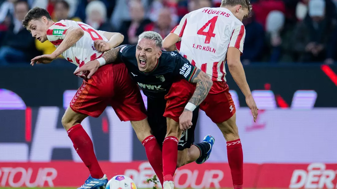 Die Kölner Eric Martel (l) und Timo Hübers (r) nehmen Augsburgs Philipp Tietz in die Zange. - Bild: Rolf Vennenbernd/dpa