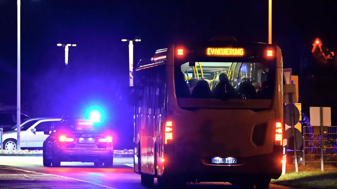 Ein Polizeiauto eskortiert einen Bus mit Menschen vom Flughafen Hamburg. - Bild: Jonas Walzberg/dpa