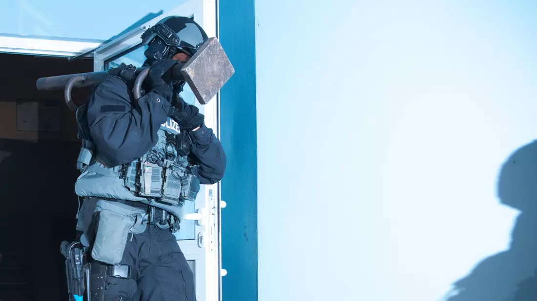 Ein Polizist verlässt bei einer Razzia ein Haus in Berlin. - Bild: Paul Zinken/dpa