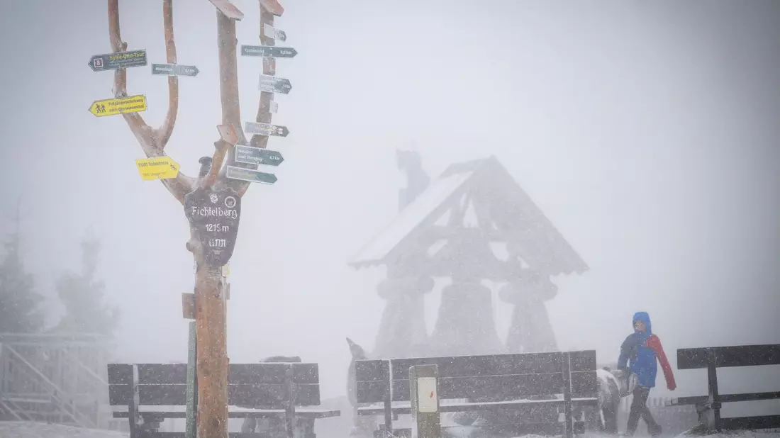 Der mit einer leichten Schneeschicht bedeckte 1215 Meter hohe Fichtelberg liegt im Nebel. - Bild: Kristin Schmidt/dpa-Zentralbild/dpa