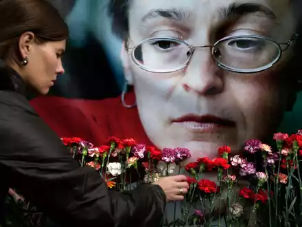Eine Frau legt in Moskau Blumen vor einem Porträt der ermordeten russischen Journalistin Anna Politkowskaja nieder (Archivbild). - Foto: Pavel Golovkin/AP/dpa