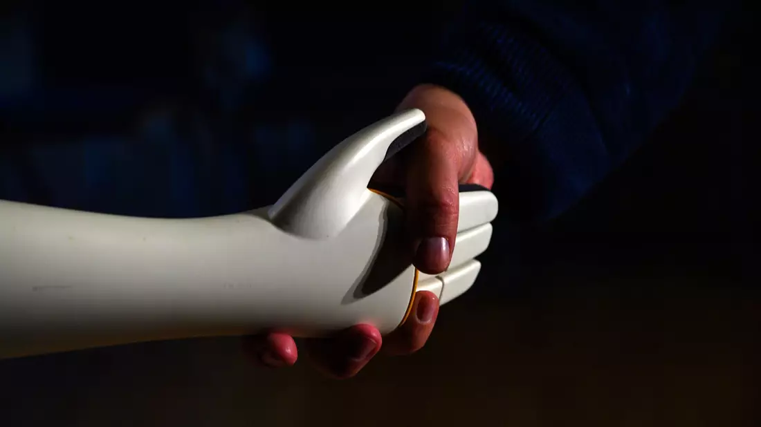 Eine menschliche Hand greift die Hand eines humanoiden Roboters. - Bild: Klaus-Dietmar Gabbert/dpa