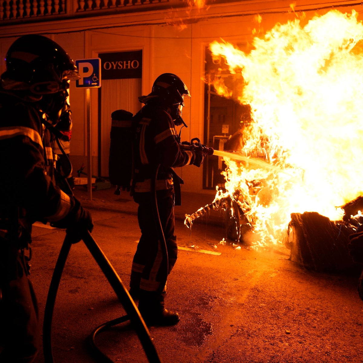 Feuerwehrleute müssen einen von Demonstranten angezündeten Müllcontainer löschen. - Foto: Manu Fernandez/AP/dpa