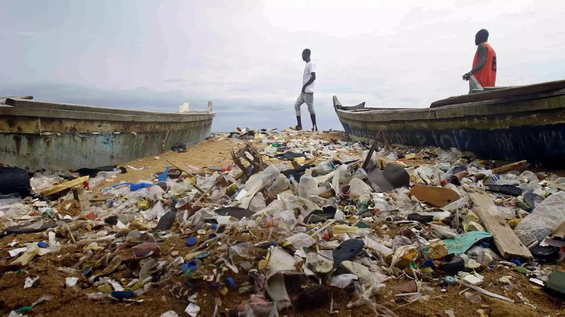 Menschen spazieren über einen mit Plastik verschmutzten Strand an der Elfenbeinküste. - Bild: Diomande Ble Blonde/AP/dpa