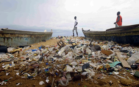 Menschen spazieren über einen mit Plastik verschmutzten Strand an der Elfenbeinküste. - Foto: Diomande Ble Blonde/AP/dpa