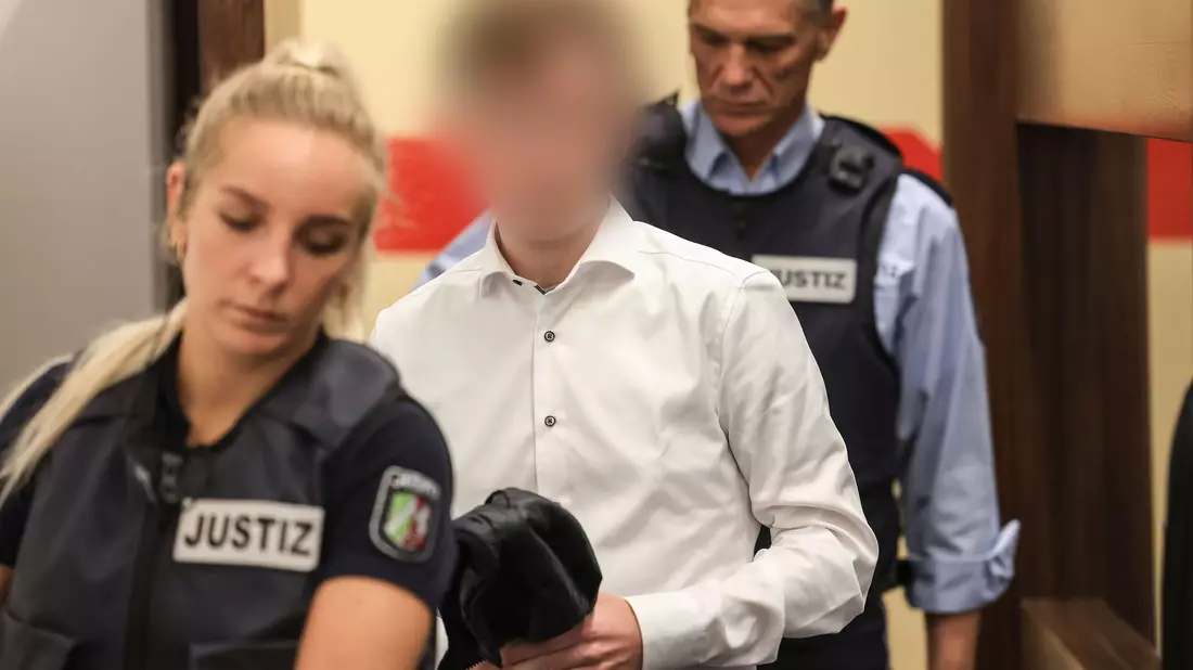 Der Angeklagte (m.) wird von Justizangestellten in den Gerichtssaal geführt. - Bild: Oliver Berg/dpa