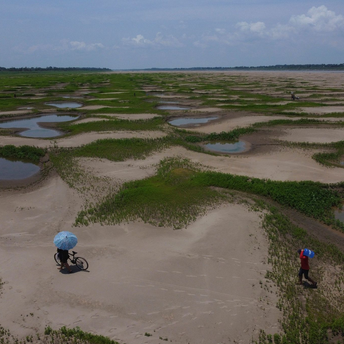 Bewohner einer Flussufergemeinde tragen Lebensmittel und Trinkwasserbehälter, die sie von der staatlichen humanitären Hilfsaktion erhalten haben. - Foto: Edmar Barros/AP/dpa
