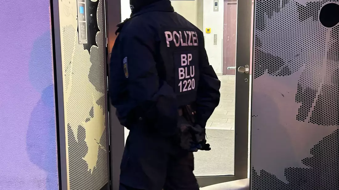 Ein Polizeibeamter steht bei einer Razzia in Berlin-Adlershof vor einem Gebäude. - Bild: Sven Kaeuler/dpa