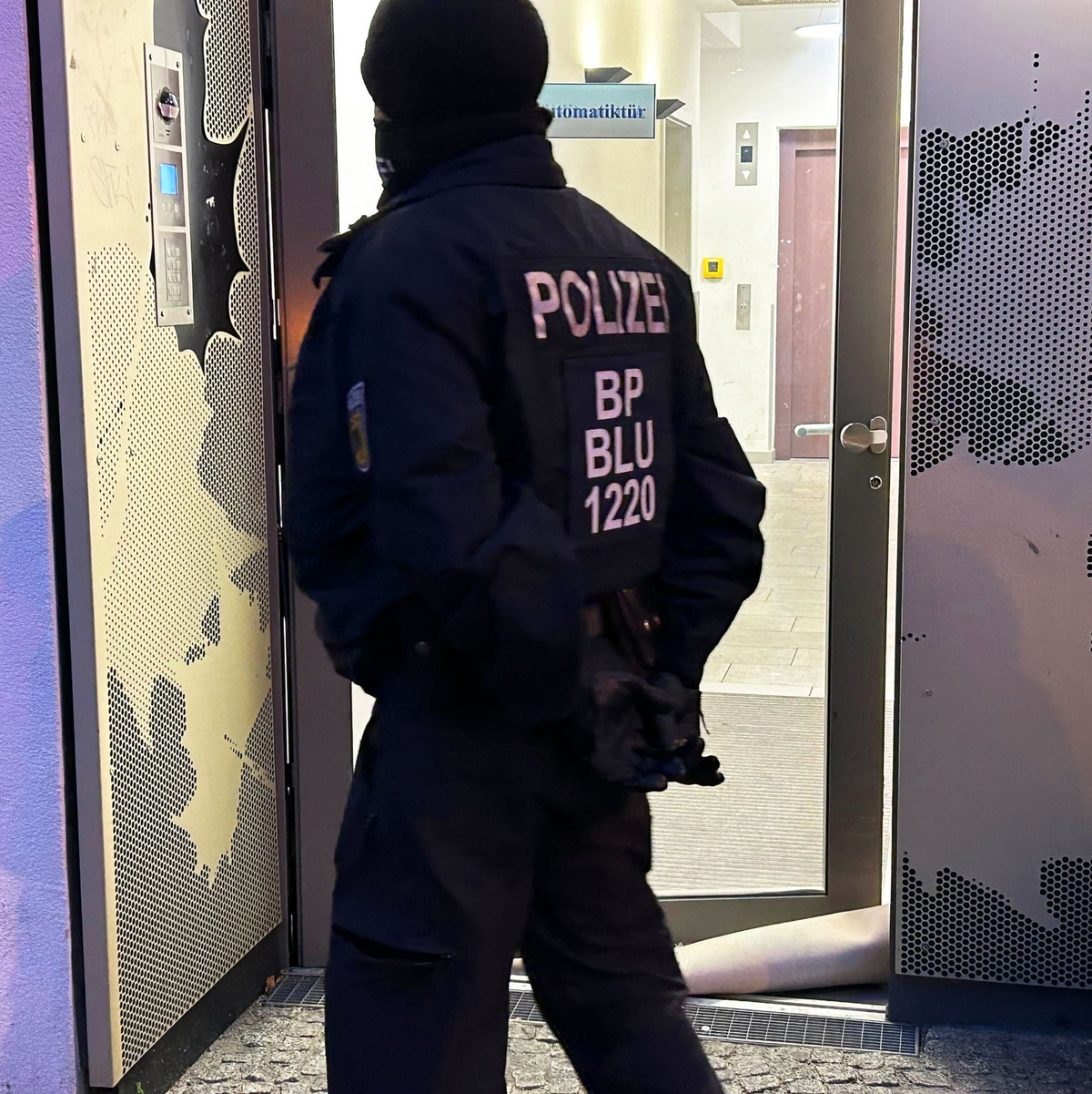 Ein Polizeibeamter steht bei einer Razzia in Berlin-Adlershof vor einem Gebäude. - Foto: Sven Kaeuler/dpa