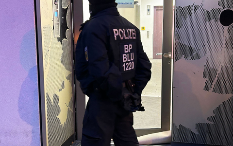 Ein Polizeibeamter steht bei einer Razzia in Berlin-Adlershof vor einem Gebäude. - Foto: Sven Kaeuler/dpa