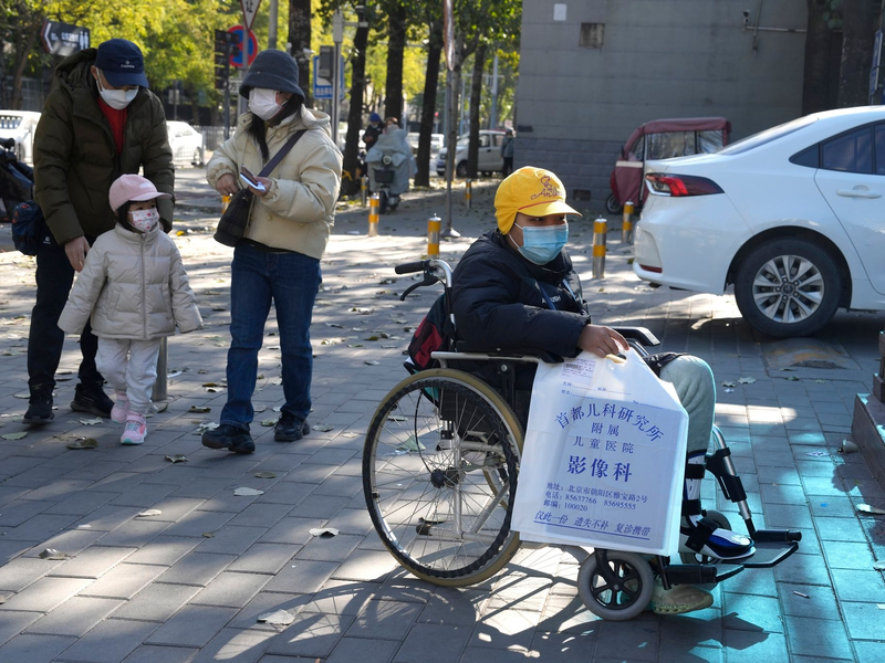 Ein Junge in einem Rollstuhl hält in Peking eine Tasche aus der radiologischen Abteilung eines Kinderkrankenhauses. In den vergangenen Tagen hatten Berichte über die starke Häufung von Atemwegserkrankungen bei Kindern Sorgen aufkommen lassen. - Foto: Ng Han Guan/AP/dpa
