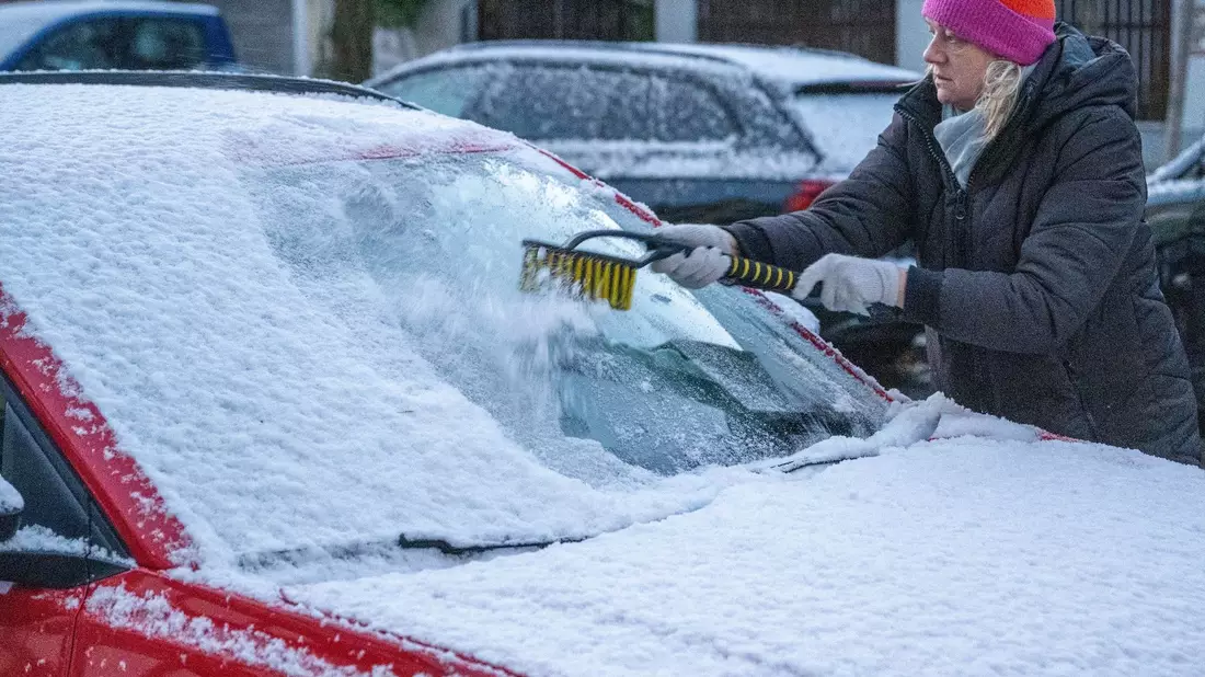 Eine Frau in München befreit am frühen Morgen ein Auto von Schnee und Eis. Auch in den kommenden Tagen soll es winterlich bleiben. - Bild: Stefan Puchner/dpa