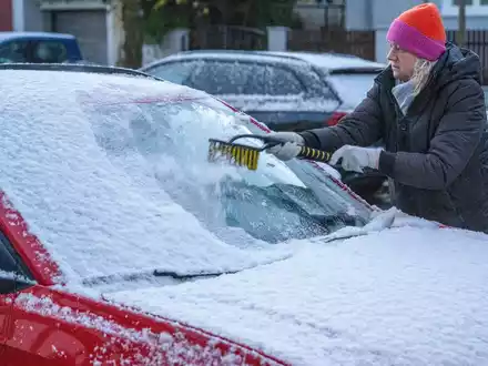 Eine Frau in München befreit am frühen Morgen ein Auto von Schnee und Eis. Auch in den kommenden Tagen soll es winterlich bleiben. - Foto: Stefan Puchner/dpa