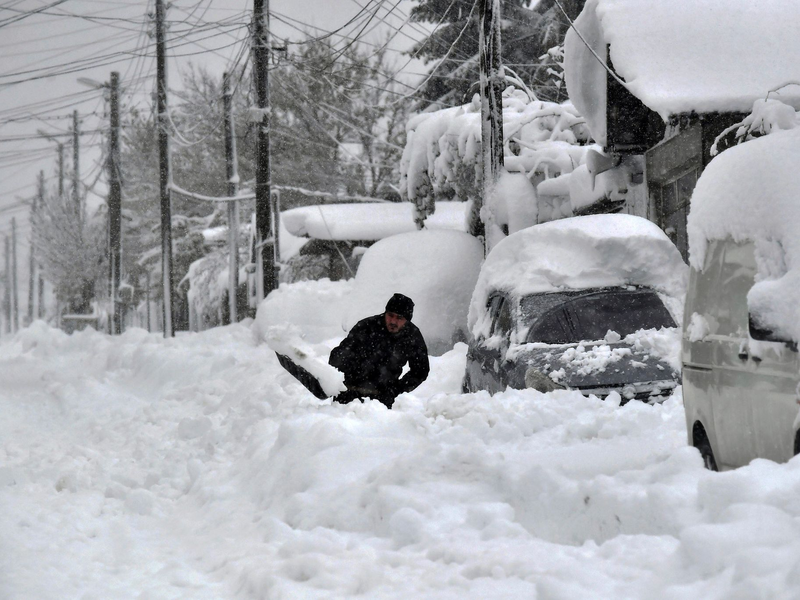 Ein Mann in Isperich schaufelt Schnee, um sein Auto zu befreien. - Foto: Mehmed Aziz/AP/dpa