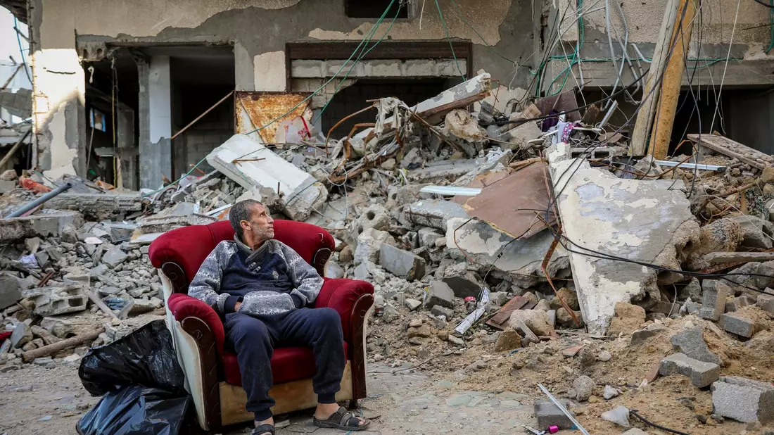 Ein palästinensischer Mann sitzt in einem Sessel vor einem zerstörten Gebäude in Gaza-Stadt. - Bild: Mohammed Hajjar/AP/dpa