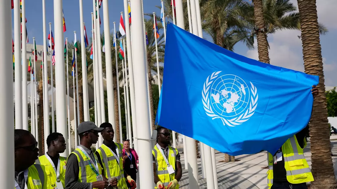 Die Flagge der Vereinten Nationen wird vor dem UN-Klimagipfel COP28 aufgehangen. - Bild: Rafiq Maqbool/AP/dpa