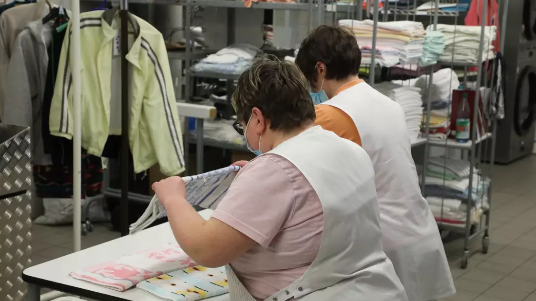 Zwei Frauen arbeiten in der Wäscherei der Lebenshilfe Gera e.V und legen dort Wäsche zusammen. - Bild: Bodo Schackow/dpa-Zentralbild/dpa