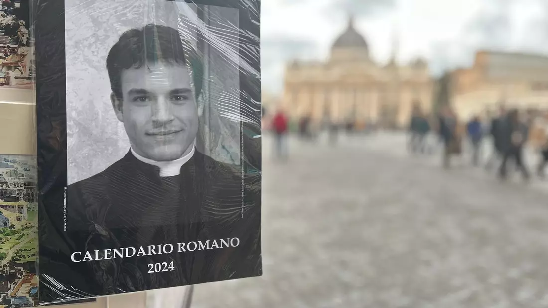 Der «Calendario Romano» an einem Souvenirstand, im Hintergrund der Petersdom. - Bild: Christoph Sator/dpa