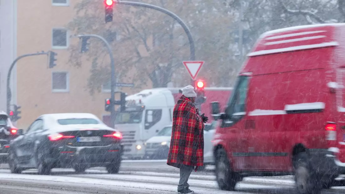Zwischen wartenden Autos an der Ampel: Bitte um Almosen bei Schneetreiben in Hamburg. - Bild: Christian Charisius/dpa