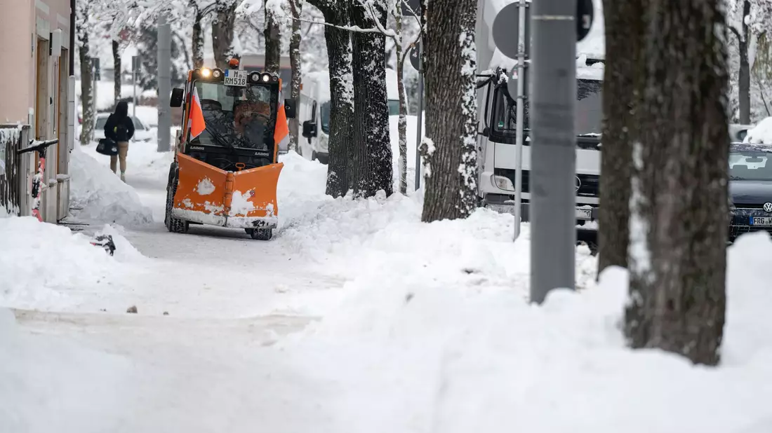Ein Räumfahrzeug fährt über einen verschneiten Weg in München. - Bild: Lukas Barth/dpa