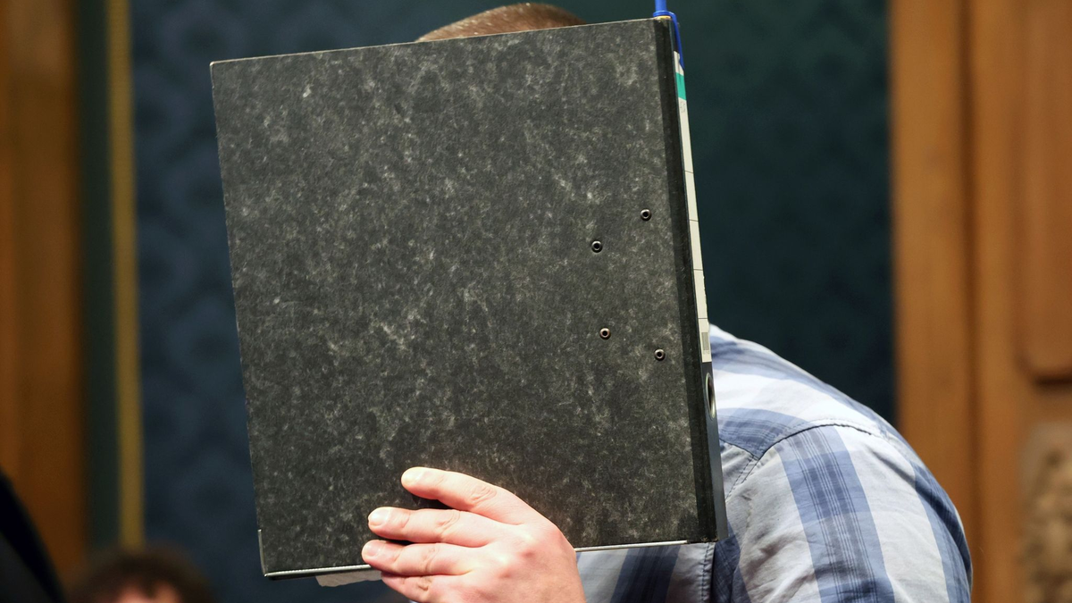 Der angeklagte Feuerwehrmann mit einem Aktendeckel vor dem Gesicht im Gerichtssaal. - Foto: Bernd Wüstneck/dpa