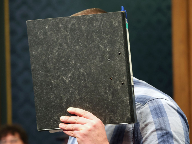 Der angeklagte Feuerwehrmann mit einem Aktendeckel vor dem Gesicht im Gerichtssaal. - Foto: Bernd WĂŒstneck/dpa