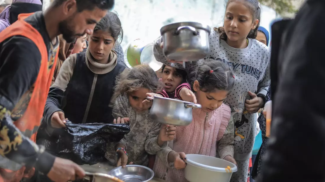 Menschen stehen in Rafah im Süden des Gazastreifens mit Töpfen, Schalen und Tüten bei einer Essensausgabe an. - Bild: Mohammed Talatene/dpa