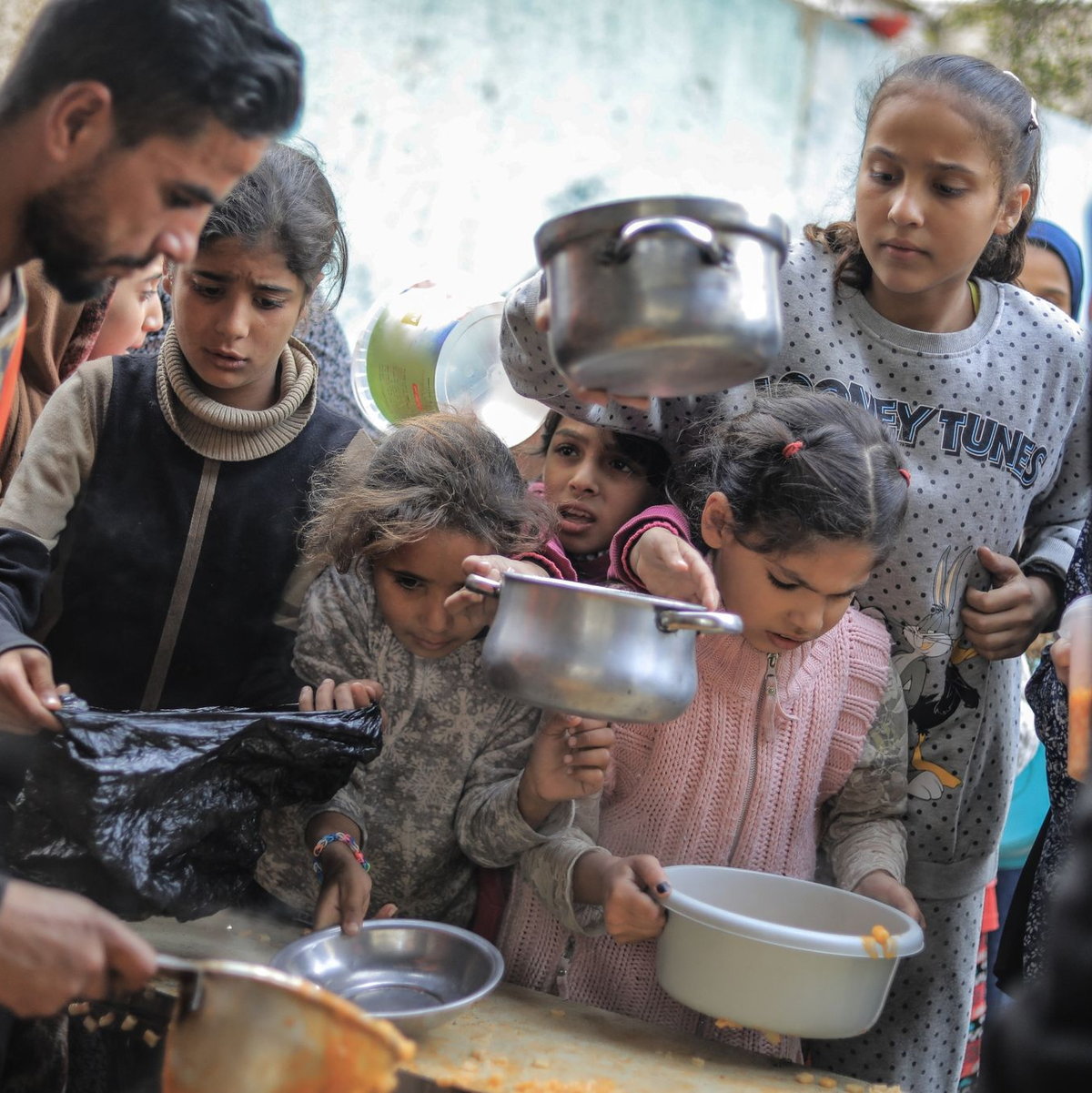 Menschen stehen in Rafah im Süden des Gazastreifens mit Töpfen, Schalen und Tüten bei einer Essensausgabe an. - Foto: Mohammed Talatene/dpa
