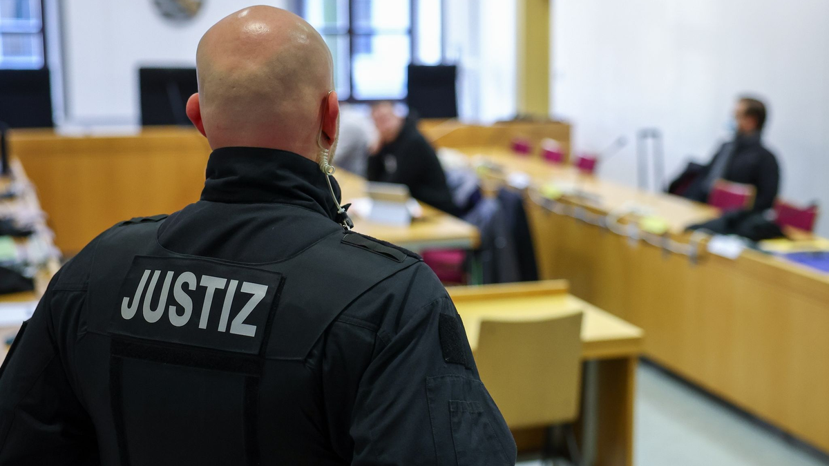 Ein Justizbeamter steht vor Prozessbeginn vor einigen Angeklagten im Landgericht Chemnitz. - Foto: Jan Woitas/dpa