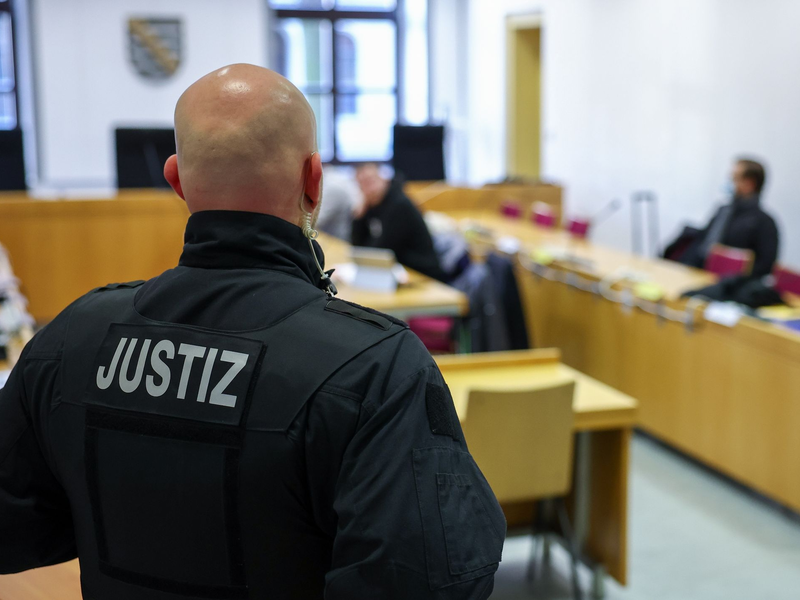 Ein Justizbeamter steht vor Prozessbeginn vor einigen Angeklagten im Landgericht Chemnitz. - Foto: Jan Woitas/dpa