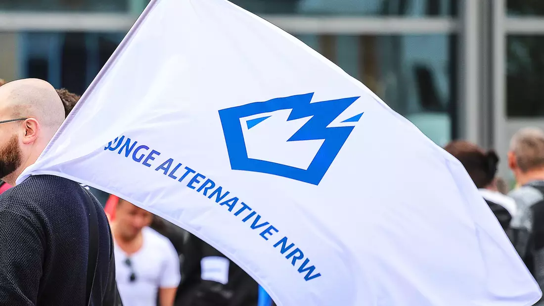 Ein Mitglied der «Jungen Alternative» (JA) trägt auf einer Wahlkampfveranstaltung in Dortmund eine Fahne mit dem Logo der Organisation. - Bild: Alex Talash/dpa
