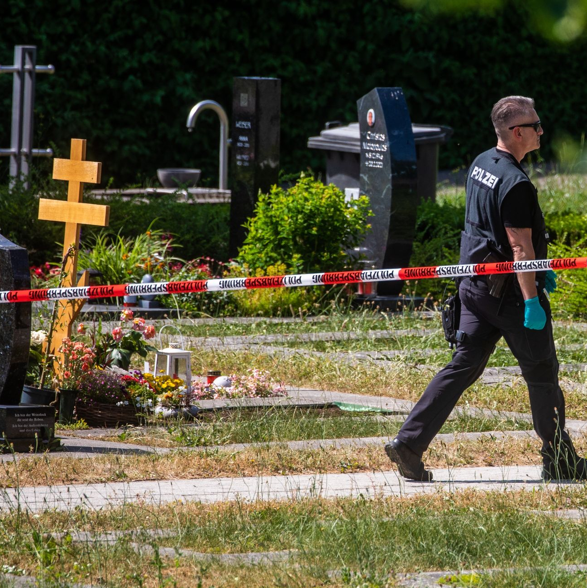 Ein Polizist geht über den abgesperrten Teil an einem Tatort auf einem Friedhof. - Foto: Christoph Schmidt/dpa