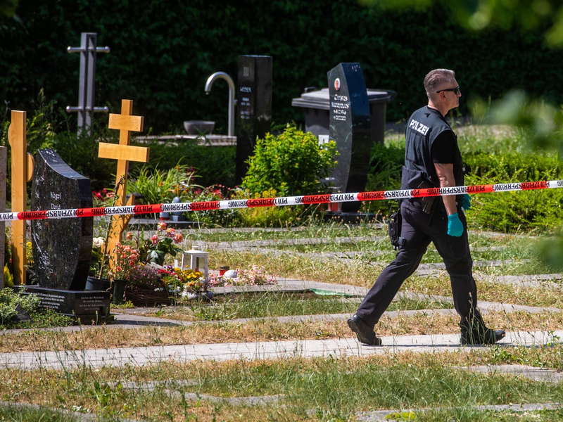 Ein Polizist geht über den abgesperrten Teil an einem Tatort auf einem Friedhof. - Foto: Christoph Schmidt/dpa