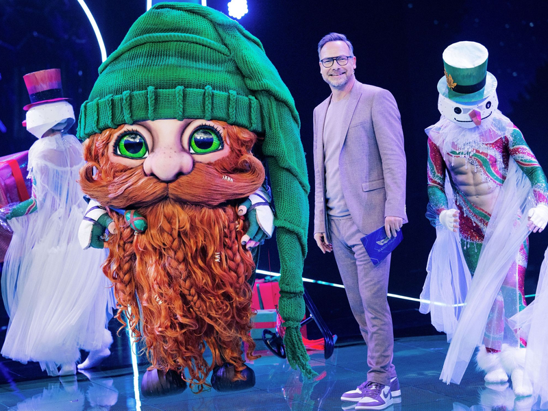 Die Figur «Klaus Claus» in der Prosieben-Show The Masked Singer neben Moderator Matthias Opdenhövel. - Foto: Rolf Vennenbernd/dpa