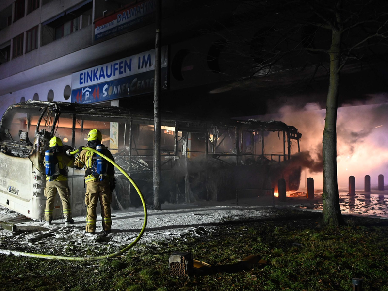 Einsatzkräfte der Feuerwehr löschen in der Silvesternacht 2022/2023 im Bezirk Berlin-Neukölln einen brennenden Bus, der von Unbekannten angezündet worden war. - Foto: Paul Zinken/dpa