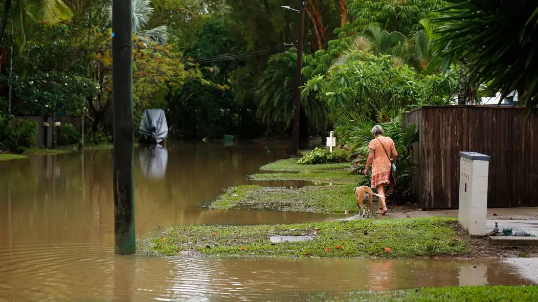 Eine Frau spaziert mit ihrem Hund durch das Hochwasser im Vorort Holloways Beach in Cairns. - Bild: Joshua Prieto/AAP/dpa