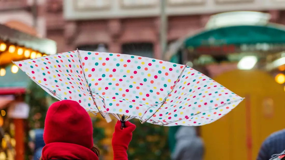Vom Wind verweht: Eine Frau geht mit einem Regenschirm über einen Weihnachtsmarkt in Frankfurt. - Bild: Andreas Arnold/dpa