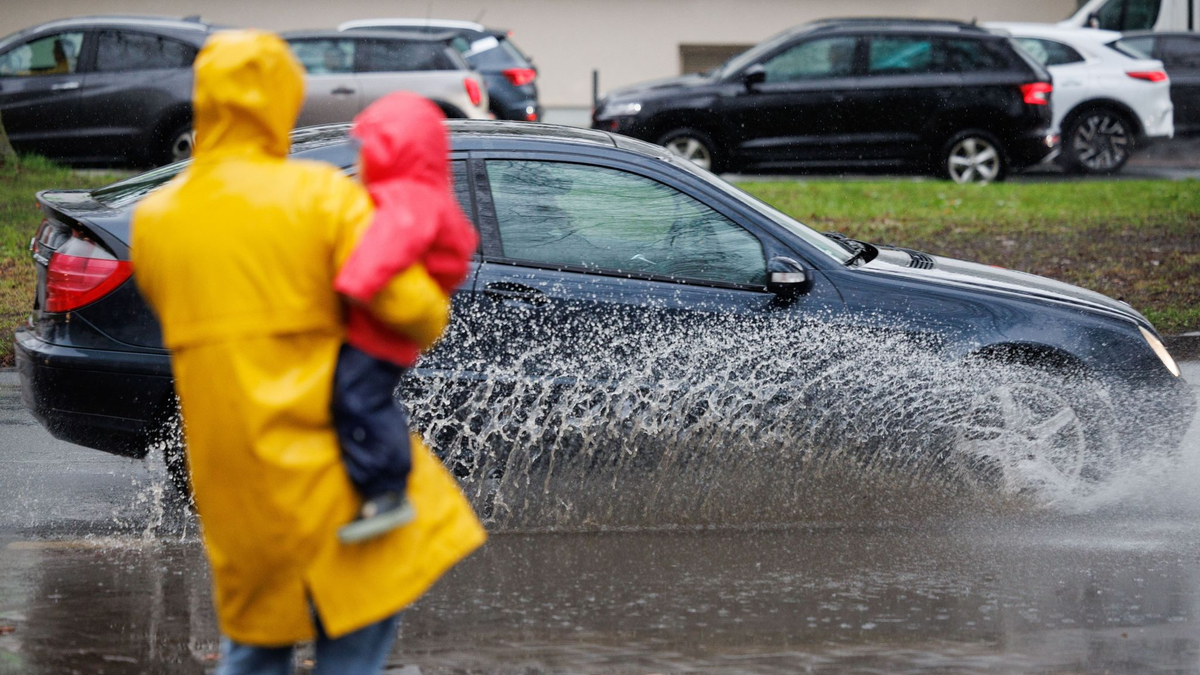 Eine Mutter und ihr Kind blicken auf eine teils überflutete Straße in Osnabrück. - Foto: Friso Gentsch/dpa